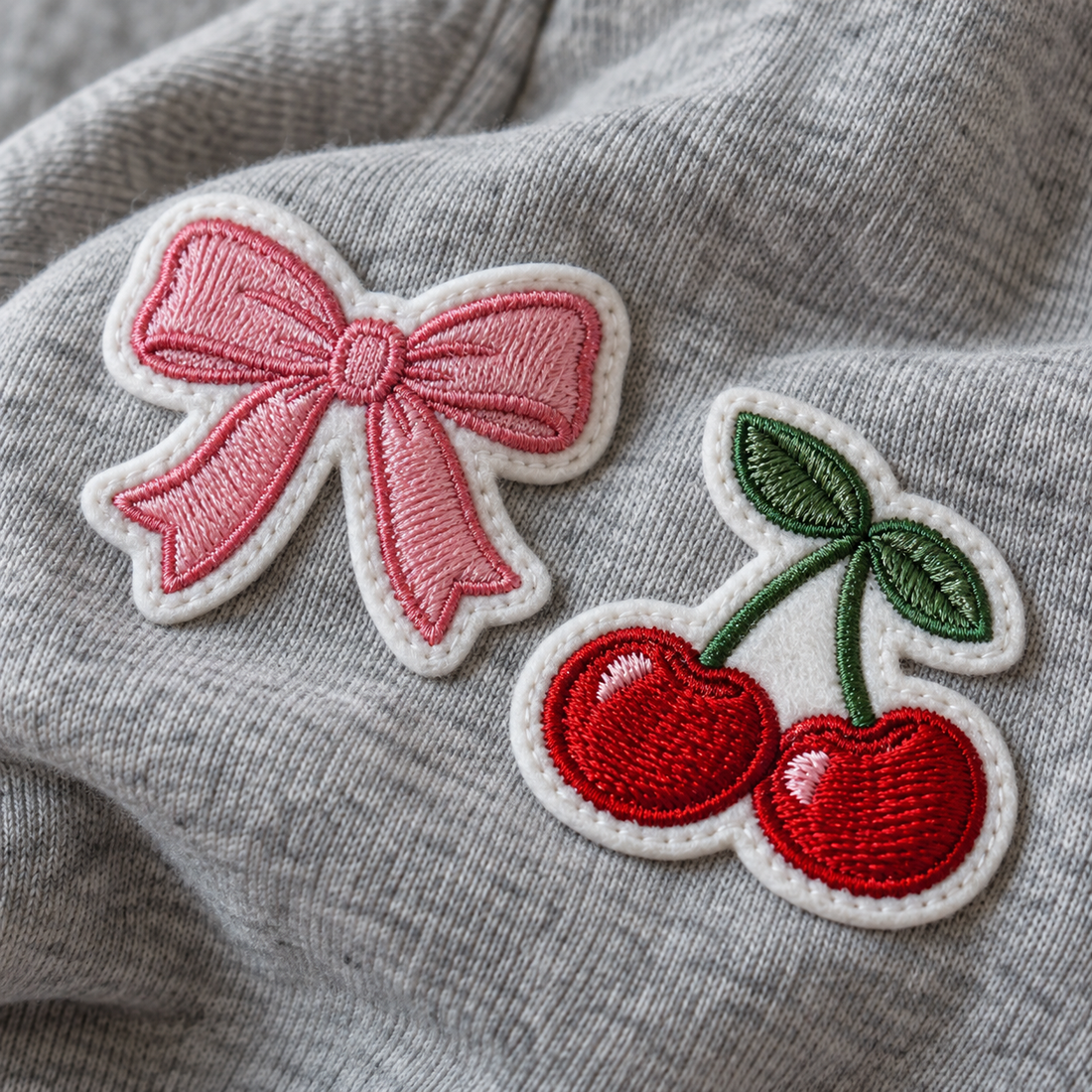 Close-up of pink bow and red cherries patches placed on a heather grey sweatshirt
