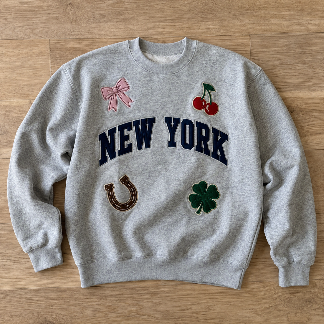Heather grey patched crewneck sweatshirt with New York, bow, cherries, horseshoe and clover patches